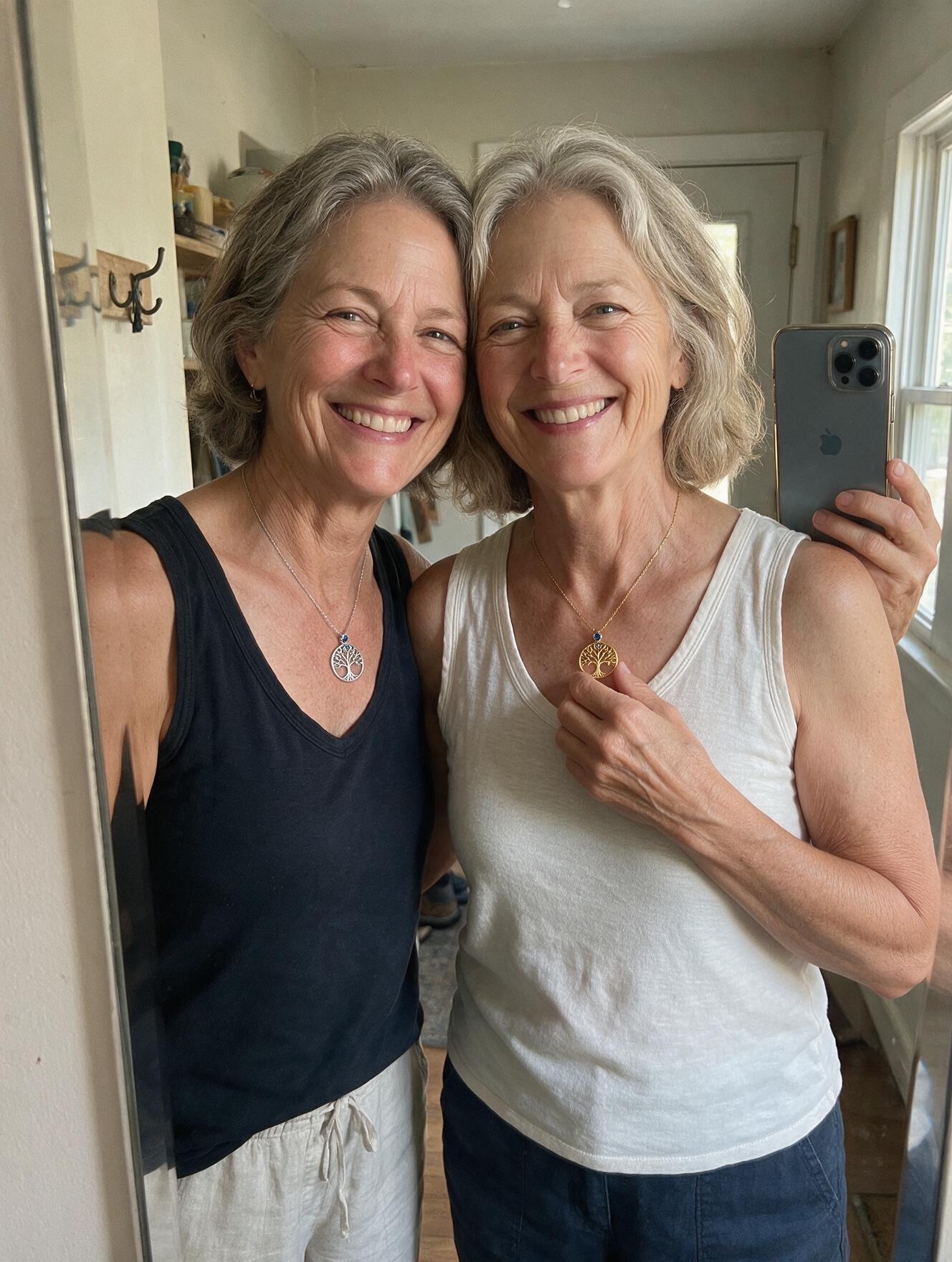 Two sisters together, both wearing the matching tree-of-life pendants — one silver, one gold